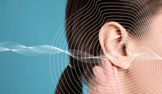 Close-up of a woman's ear with sound wave graphics overlay. The background is a solid blue, and the woman's hair is tied back, emphasizing the ear. The waves suggest sound or hearing concepts.